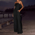 Woman wearing elegant black losse tube-top jumpsuit standing on wooden pier at dusk