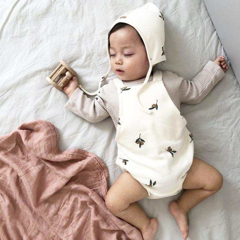 Baby in zachte katoenen westerse kleding met muts en romper met print liggend op bed