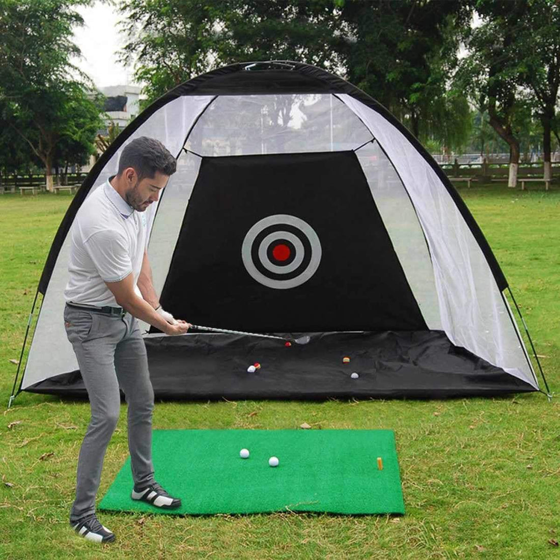 Man practicing golf swing in a black and green golf oefennet tent with target net on outdoor grass field