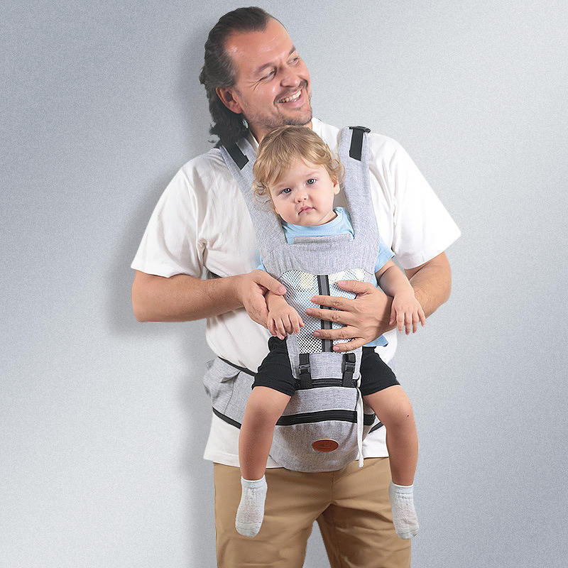Vader draagt peuter in grijze ergonomische baby heupstoel drager met verstelbare riemen en zachte binnenkant.