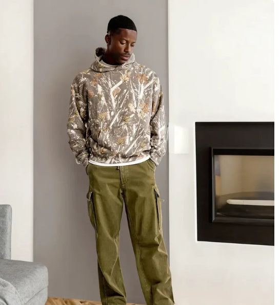 Man wearing casual damestop met zakken hoodie with plant and flower print and olive green pants indoors