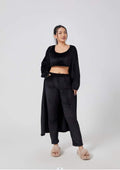 vrouwelijk model in zwarte zachte 3-delige loungewear set met crop top, broek en lange cardigan