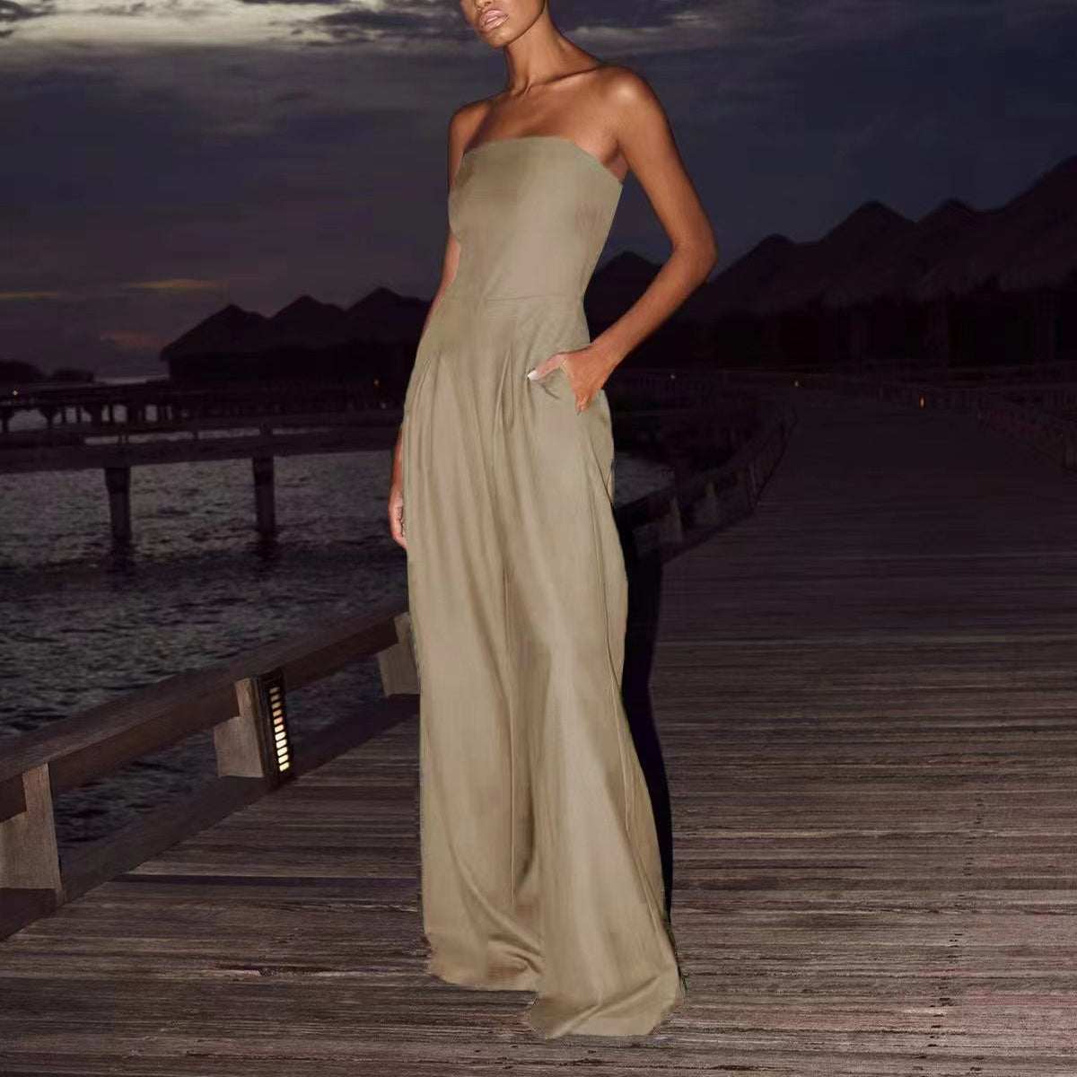 Woman wearing loose beige tube-top jumpsuit standing on wooden pier at dusk
