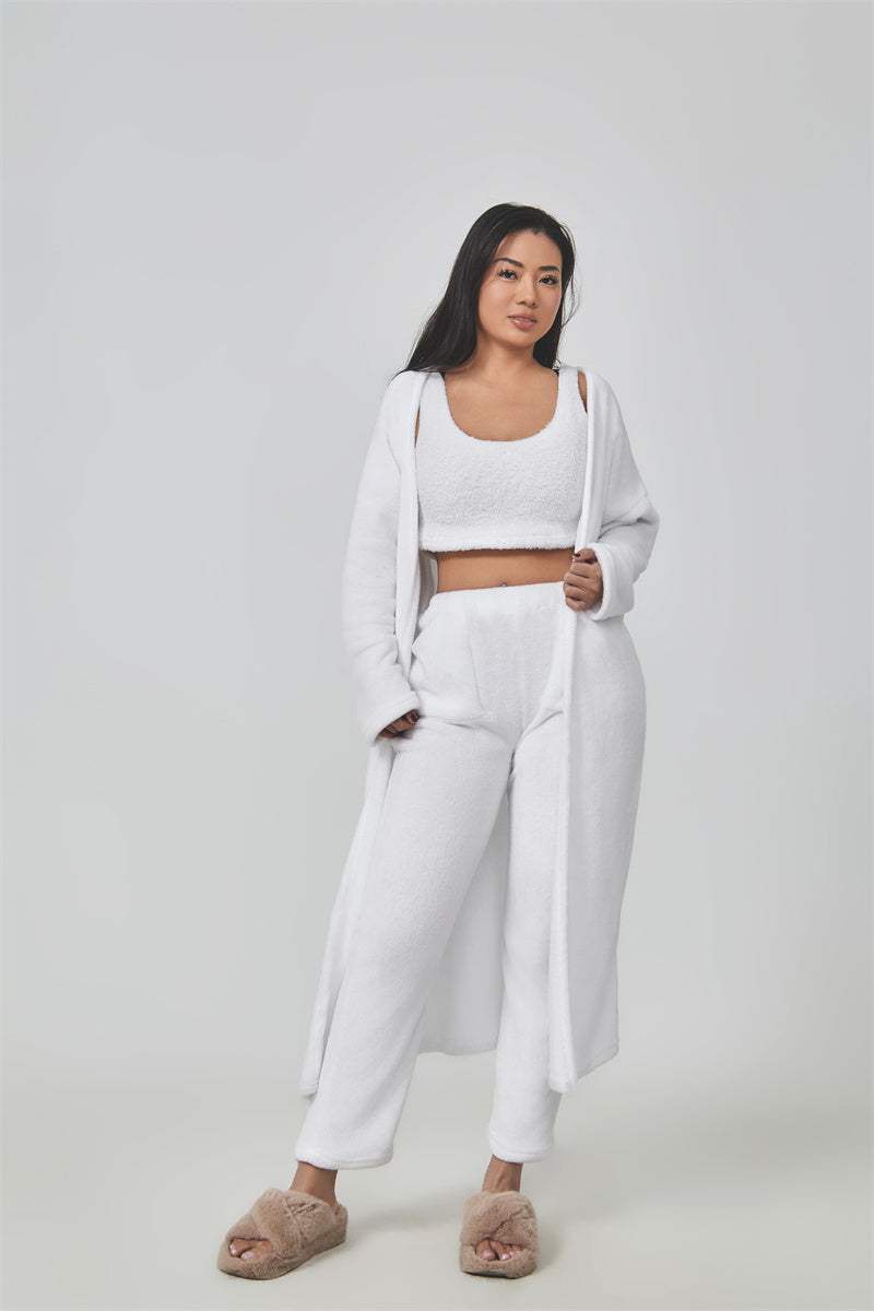 Vrouwelijk model draagt zachte witte 3-delige set met crop top, lange cardigan en broek met brede pijpen.
